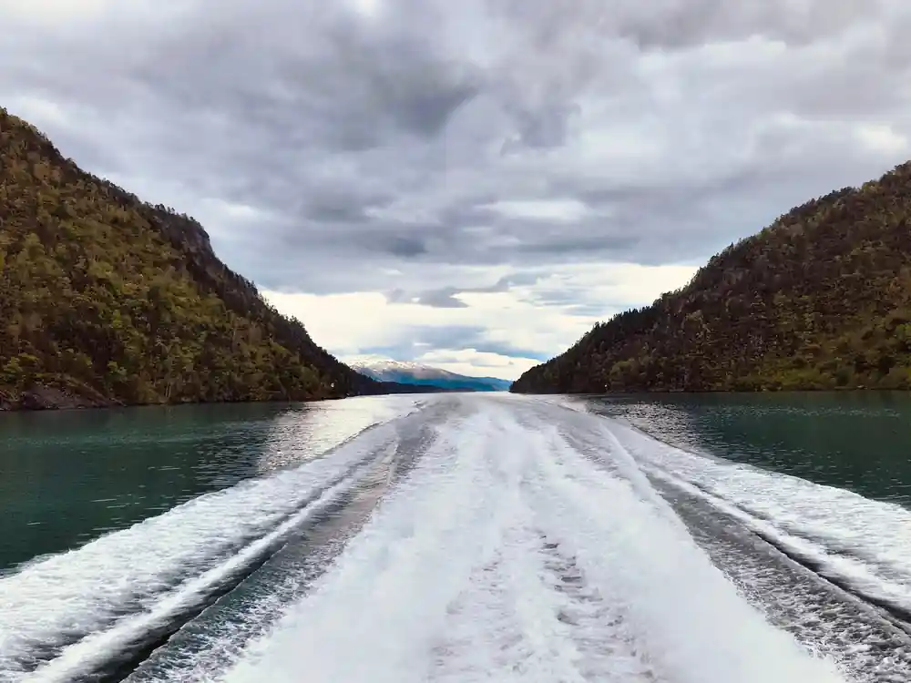 the boat wake running back down a fjord under heavy grey cloud