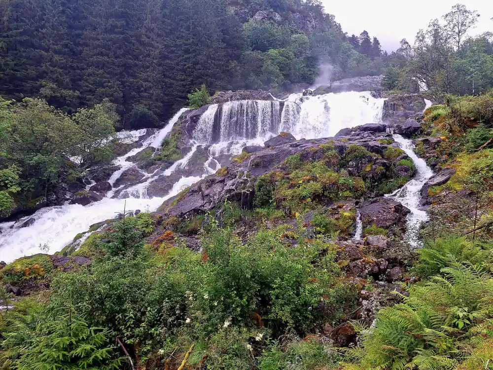 a broad waterfall over dark rock beside the path