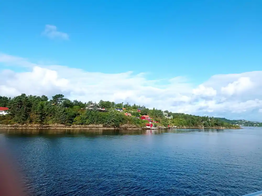 a calm blue fjord inlet with wooded islets and a red boathouse