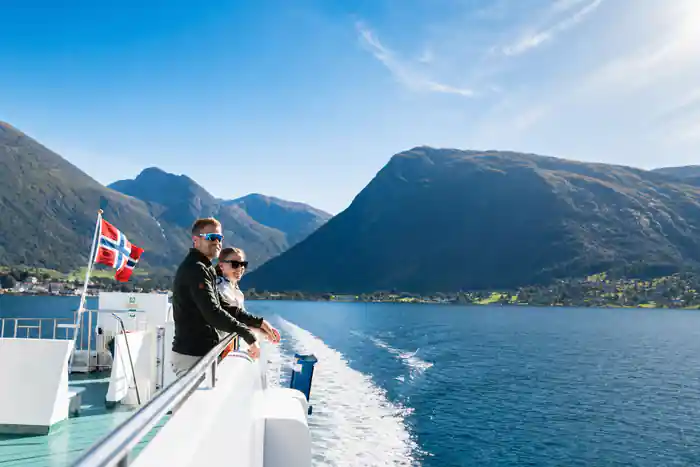 two passengers at the stern rail watching the wake with fjord mountains behind