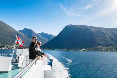 two passengers at the stern rail watching the wake with fjord mountains behind