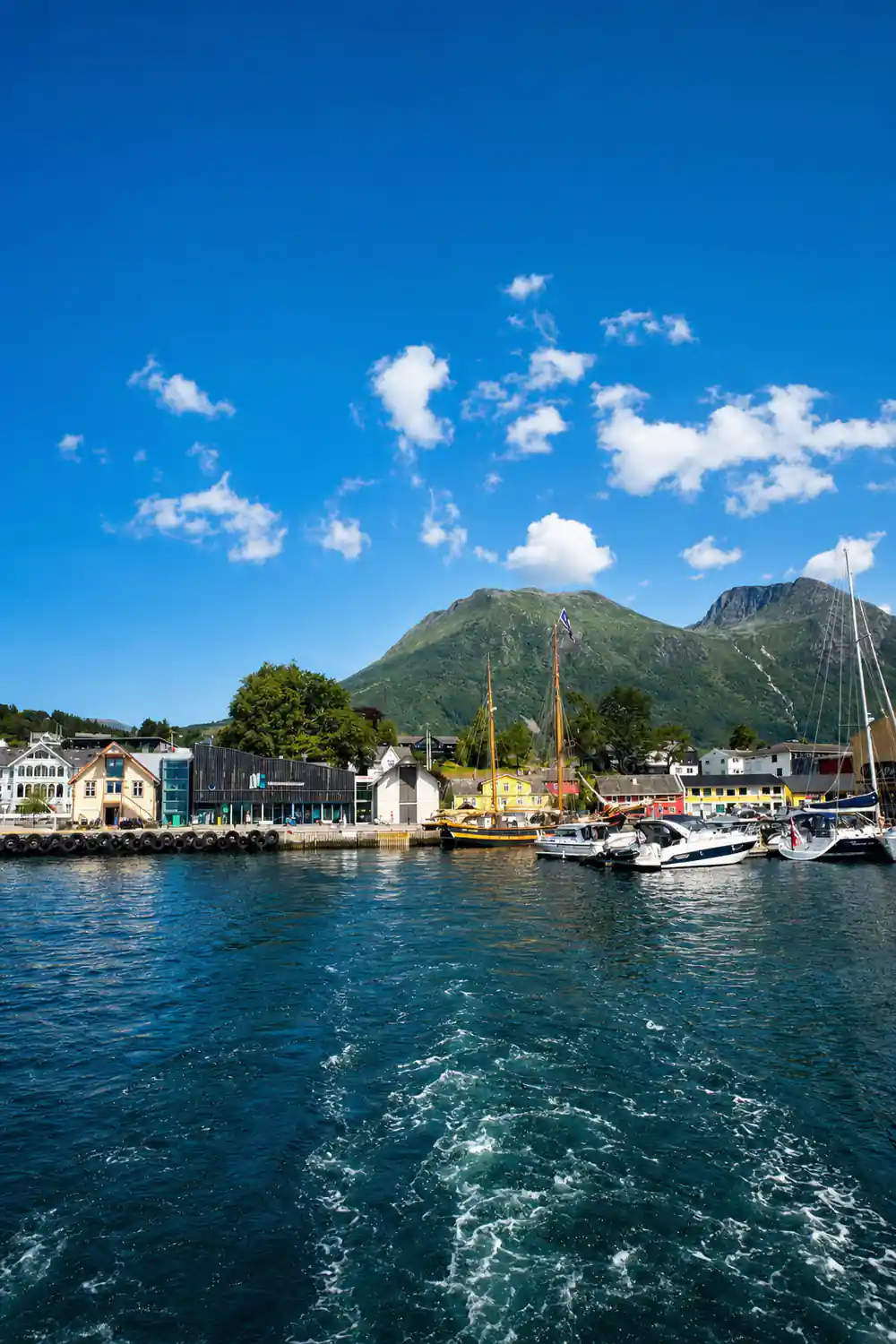 the wake curving away from a small fjord town with boats at its quays