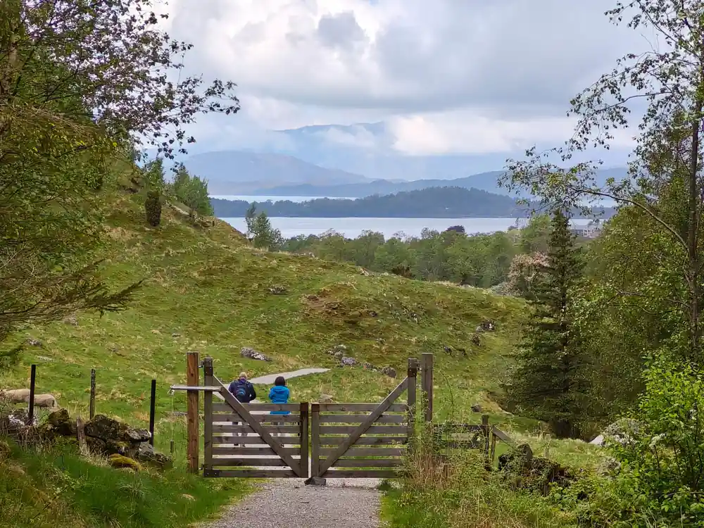 a walker at a field gate on the path with the fjord below