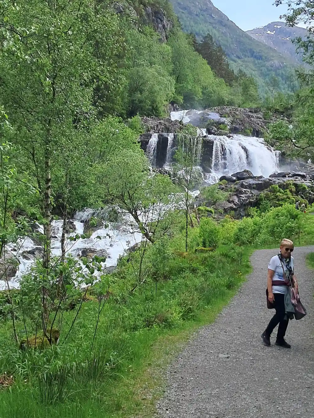 a walker on the gravel path beside the falls above the village