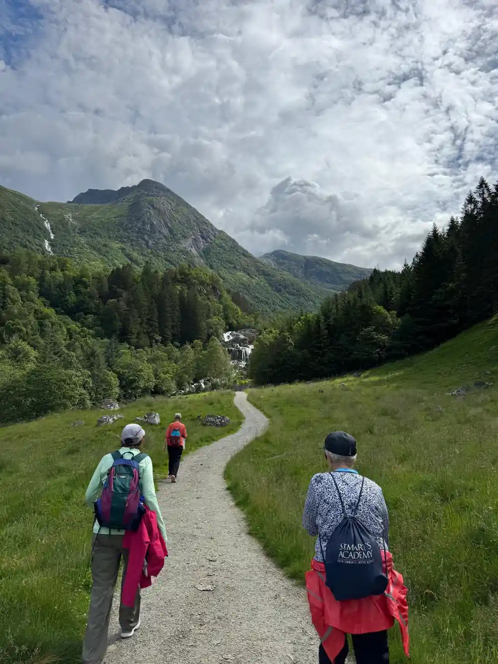 walkers on a hill path heading up the valley towards the tops