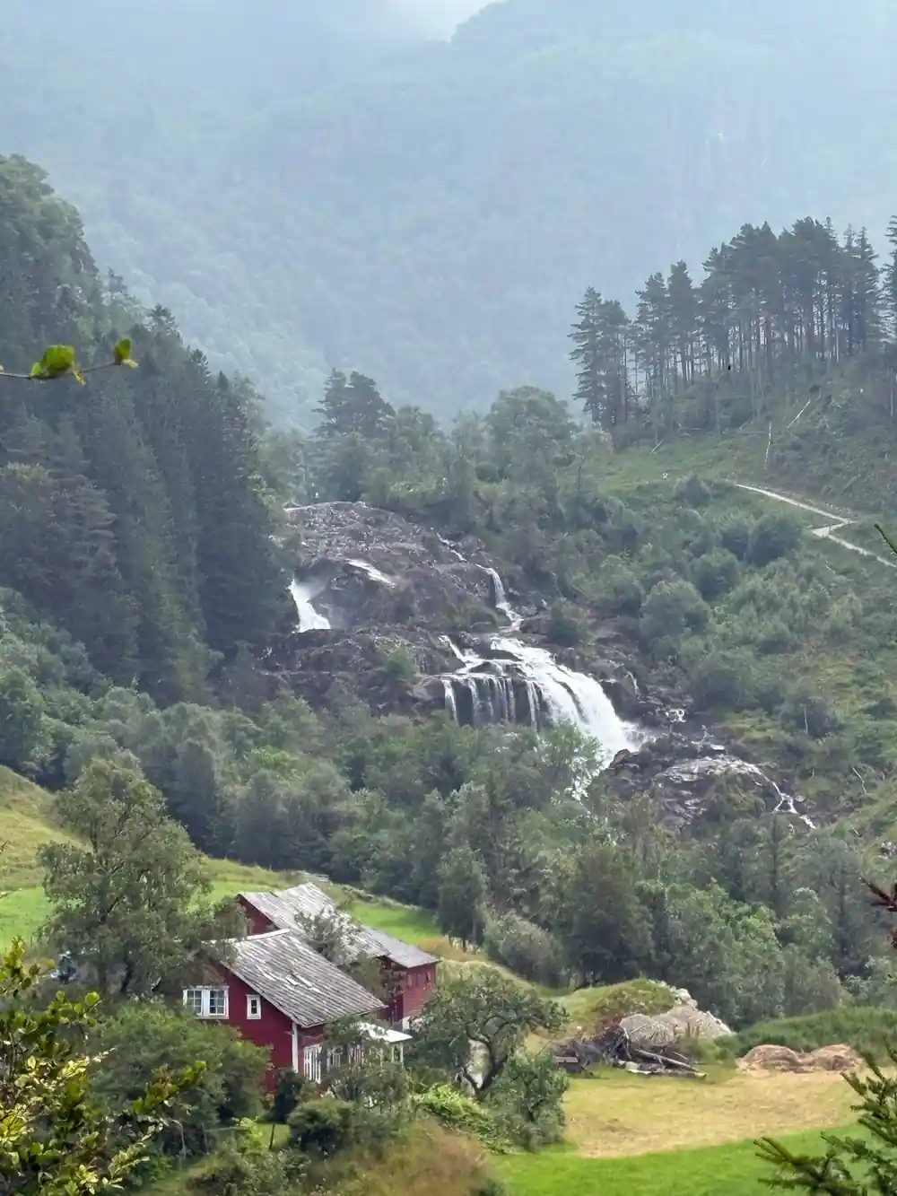 a waterfall in fine rain above red-roofed farm buildings