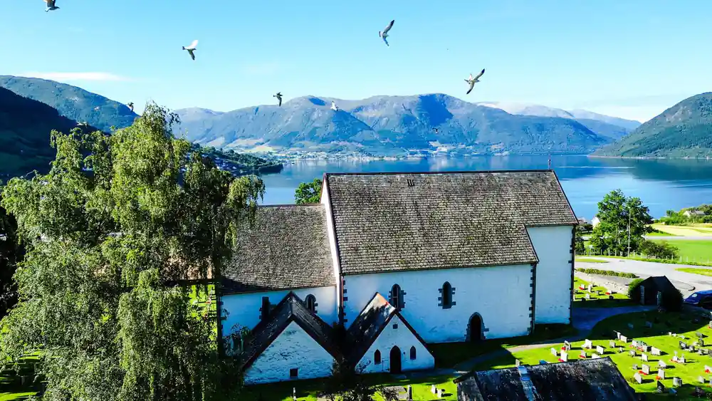 a white stone church with a slate roof above the fjord, gulls overhead