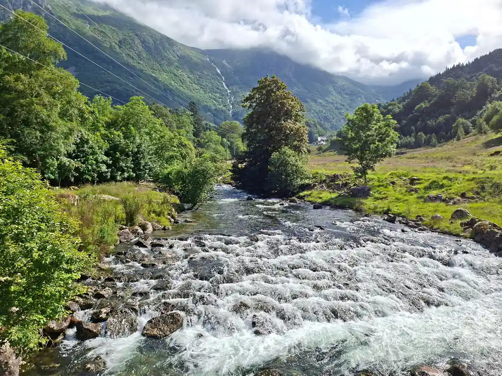 a wide shallow river running over stones below green mountains