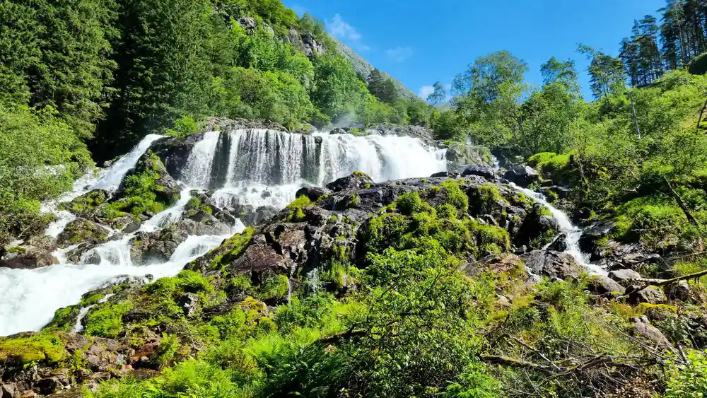 a wide waterfall spilling over mossy rock beside a green hillside